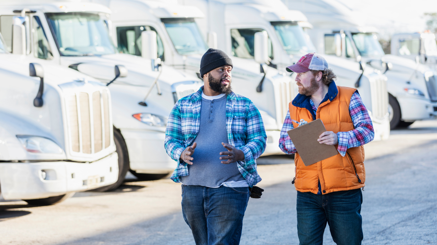 two truckers walking and talking down a row of parked long-haul trucks
